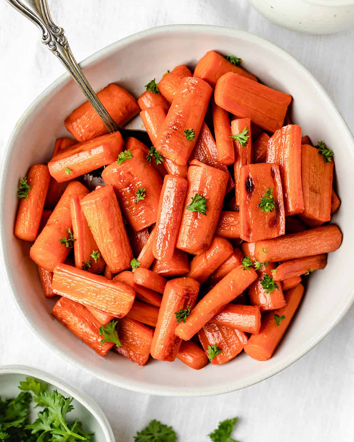 Honey Roasted Carrots are an addicting vegetable side dish perfect for any occasion! This honey carrots recipe only has 5, good-for-you ingredients and is super easy to make! honey glazed carrots in a bowl garnished with carrot greens.