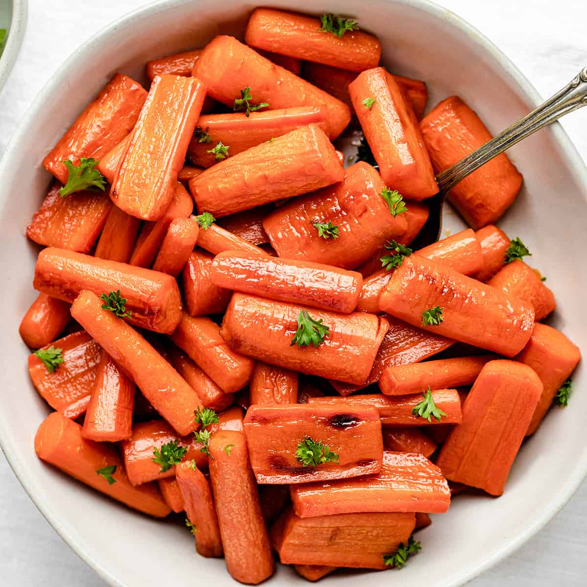 Honey Roasted Carrots in a white bowl garnished with carrot greens