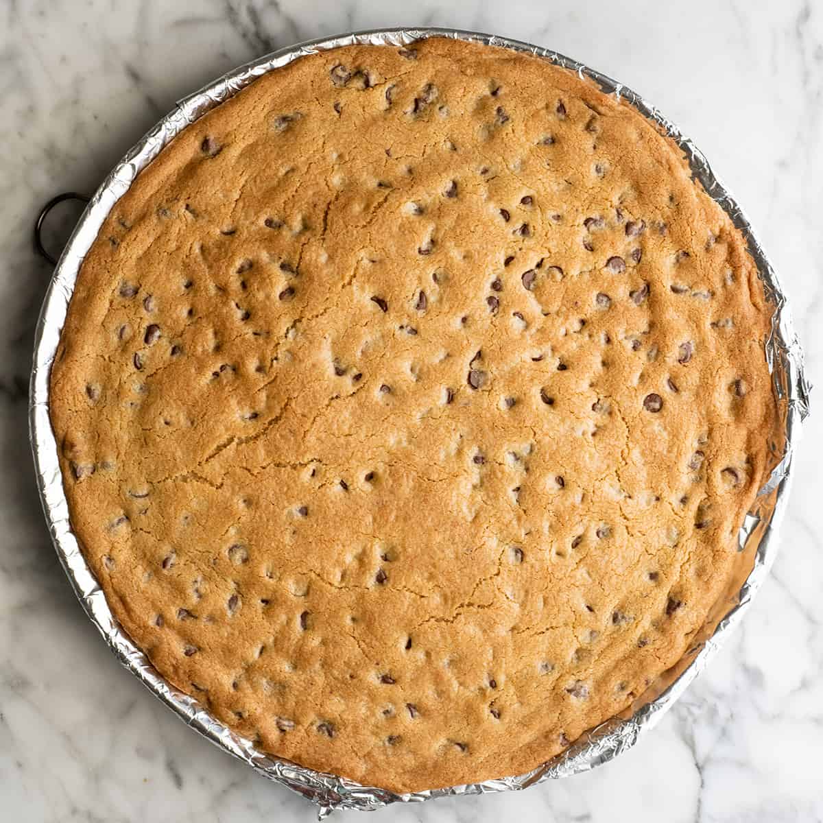 This chocolate chip cookie cake recipe is soft, chewy, slightly doughy and decorated with the best chocolate buttercream frosting. It's easy to make, large enough to feed a crowd, and even better than store-bought! chocolate chip cookie cake on a baking sheet after baking