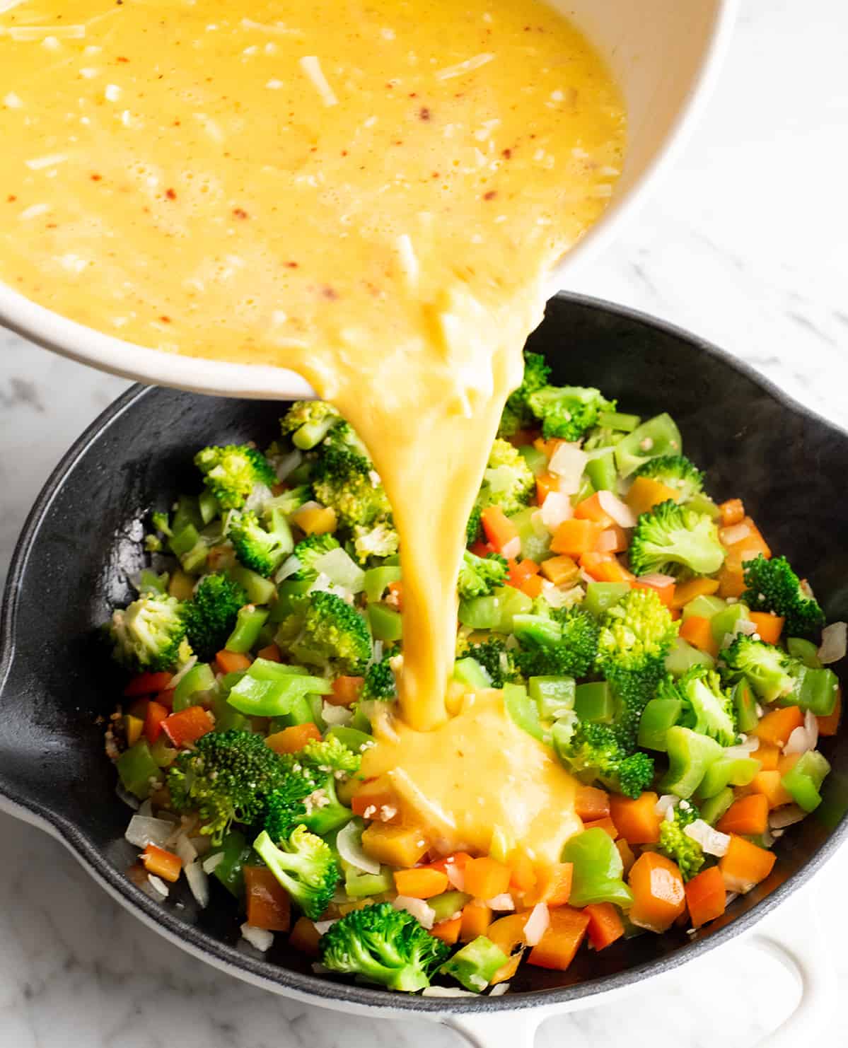 This easy Frittata Recipe is the perfect quick & healthy dinner, breakfast or brunch! Follow our step-by-step instructions and watch the video to learn how to make either a vegetable frittata or a frittata with bacon! photo showing how to make a frittata recipe pouring egg mixture into cooked vegetables