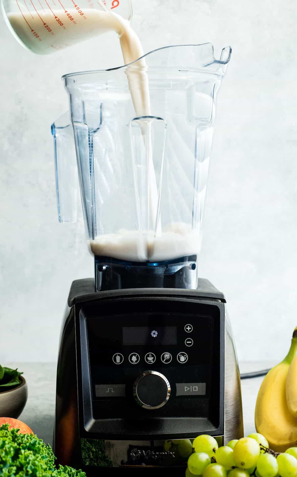 How to make the best green smoothie recipe! A simple green smoothie for beginners that is healthy, tastes amazing, and it's made with 4 ingredients in less than 5 minutes! Plus my tips on meal prepping smoothies! #greensmoothie #smoothie #smoothierecipe #greensmoothierecipe #kidfriendly front view of almond milk being poured into the Vitamix A3500 blender to make this Green Smoothie Recipe