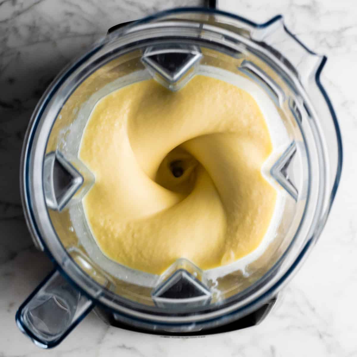 This healthy Pineapple Smoothie recipe is easy to make with only 5 ingredients in 5 minutes! One sip of this pineapple banana smoothie will make you feel like you're on a tropical island, it's like a beach vacation in a glass! Plus it's dairy-free! #pineapple #smoothie #pineapplesmoothie #banana #joyfoodsunshine #smoothierecipe overhead view of pineapple smoothie blending in a vitamix blender