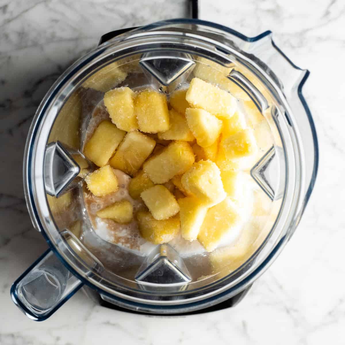This healthy Pineapple Smoothie recipe is easy to make with only 5 ingredients in 5 minutes! One sip of this pineapple banana smoothie will make you feel like you're on a tropical island, it's like a beach vacation in a glass! Plus it's dairy-free! #pineapple #smoothie #pineapplesmoothie #banana #joyfoodsunshine #smoothierecipe overhead view of how to make a pineapple smoothie in a Vitamix blender
