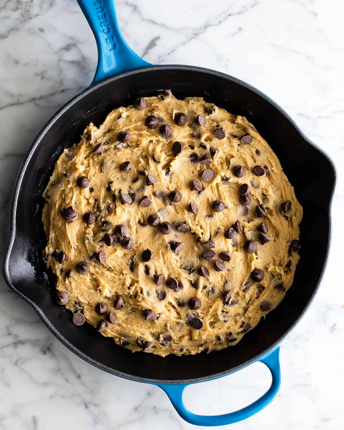 The BEST Chocolate Chip Skillet Cookie recipe! This ooey gooey, warm & melty skillet cookie (AKA: Pizookie) is completely irresistible. It's like eating warm cookie dough topped with vanilla ice cream, better than any restaurant version you've ever had! Plus it's easy to make & comes together in 20 minutes flat! #skilletcookie #pizookie #chocolatechipcookie #dessert #baking #joyfoodsunshine overhead view of skillet cookie batter in a skillet before baking