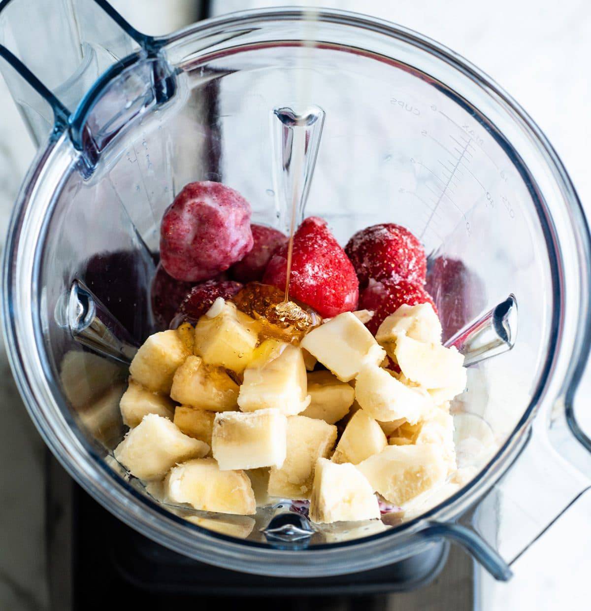 Follow our step-by-step photos & video to learn how to make the BEST easy & healthy smoothie bowl recipe (3 varieties) with 5 ingredients in 5 minutes! Smoothie bowls make the best breakfast, brunch or snack, and you can save so much money making them at home! Paleo, dairy-free and vegan-friendly. overhead photo showing how to make a smoothie bowl - adding honey