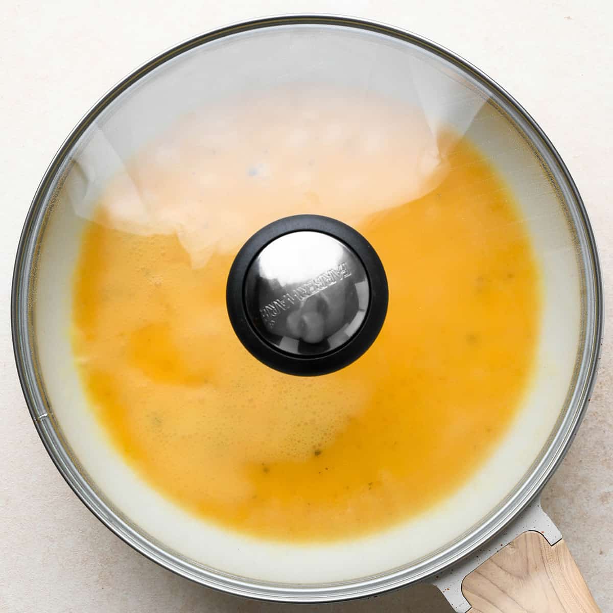 an omelette cooking in a pan with the lid on