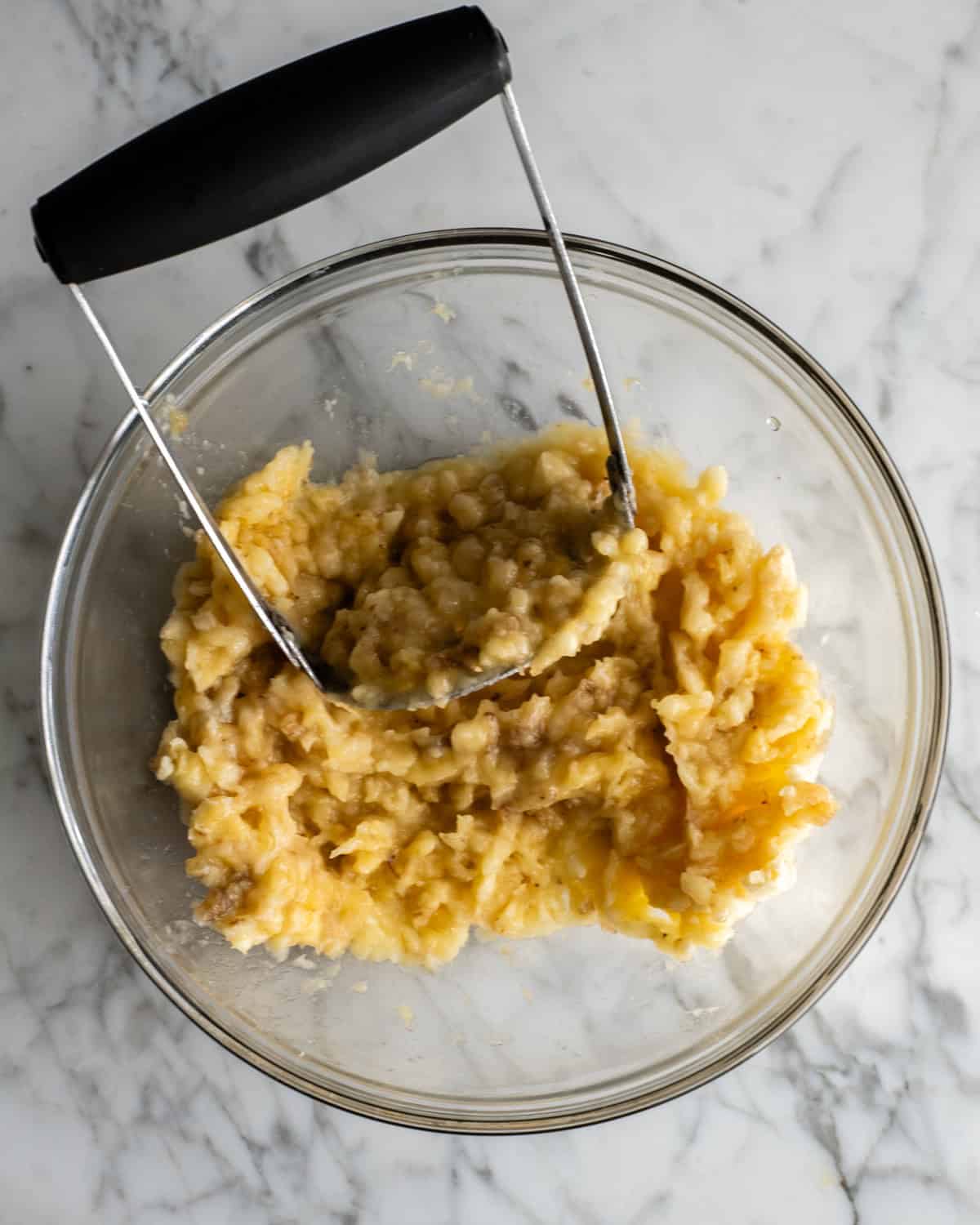 This is the best banana cake recipe ever! It's easy to make (no mixer required), moist, loaded with bananas and topped with a delicious cream cheese frosting. mashed banana in a glass bowl with a potato masher