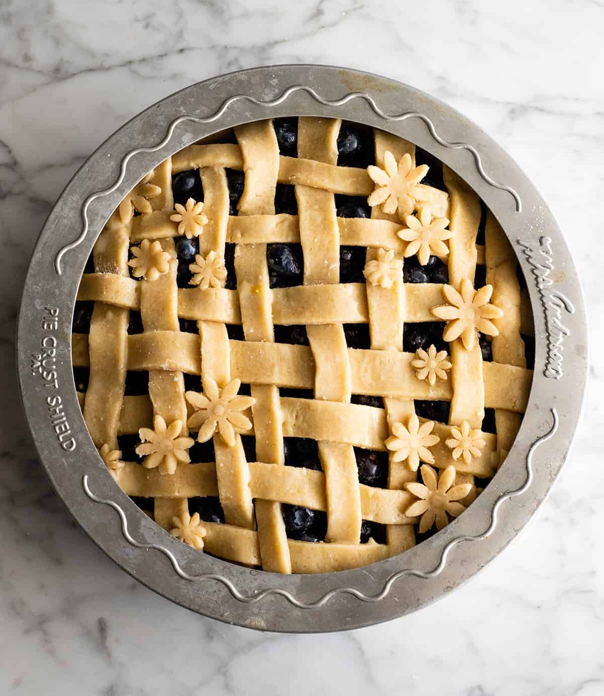 This is the best homemade Blueberry Pie Recipe you'll ever make! It's made from scratch with a fresh blueberry pie filling and NO cornstarch, and includes step-by-step instructions and photos! overhead view of a blueberry pie before baking with a pie crust shield around the edge