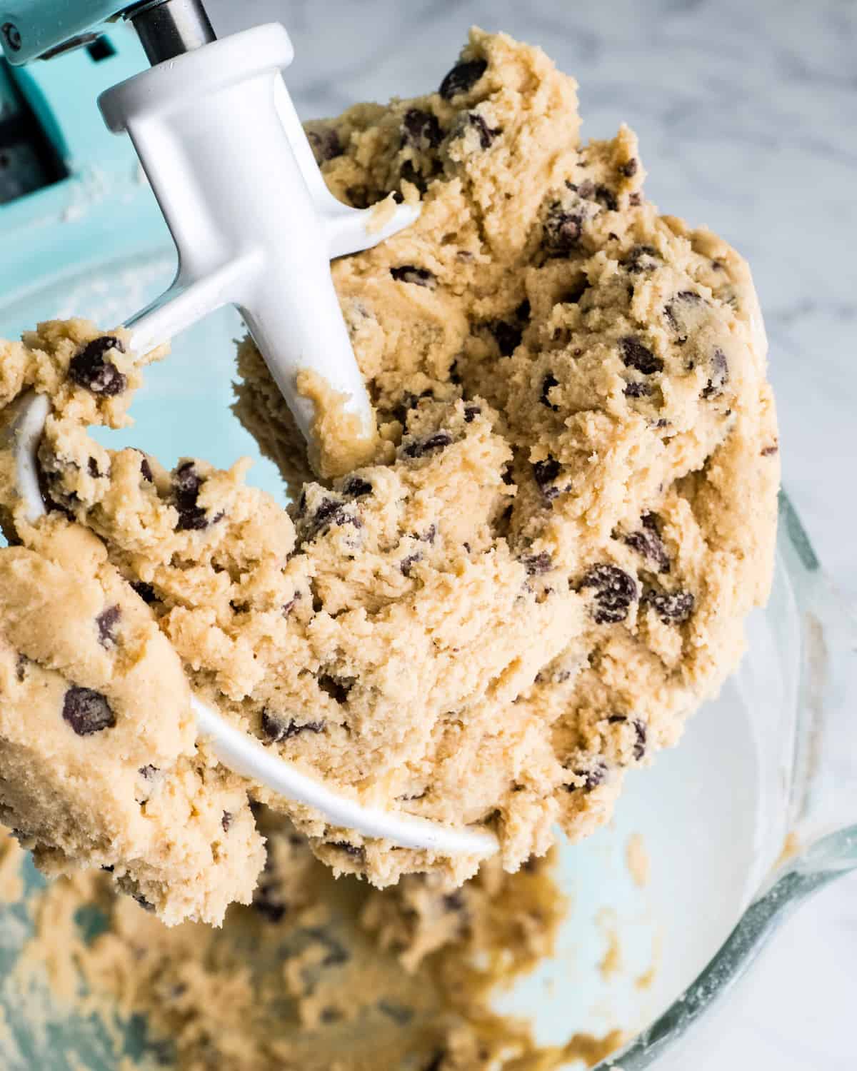 These are the absolute best chocolate chip cookie bars EVER. This cookie bar recipe is easy to make (5 minutes to mix, 20 minutes to bake) and results in a gooey, chewy, doughy yet fully cooked chocolate chip cookie bar that is 100% irresistible. Serve warm with a scoop of ice cream! #chocolatechipcookiebars #cookiebars #cookeis #dessert #baking overhead view of chocolate chip cookie bar dough in a standing mixer