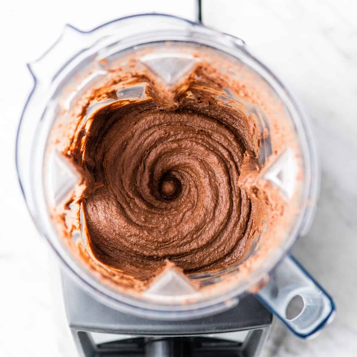 Healthy Chocolate Hummus Recipe is easy to make and ready in 5 minutes! It's a nutritious dip, appetizer, dessert, snack or spread that everyone in my family, including my kids, loves. This dessert hummus recipe is gluten-free, dairy-free, has no refined sugar & it's vegan! #hummus #chocolatehummus #vitamix #desserthummus #vegan Overhead view of a vortex of Chocolate Hummus in the Vitamix blender