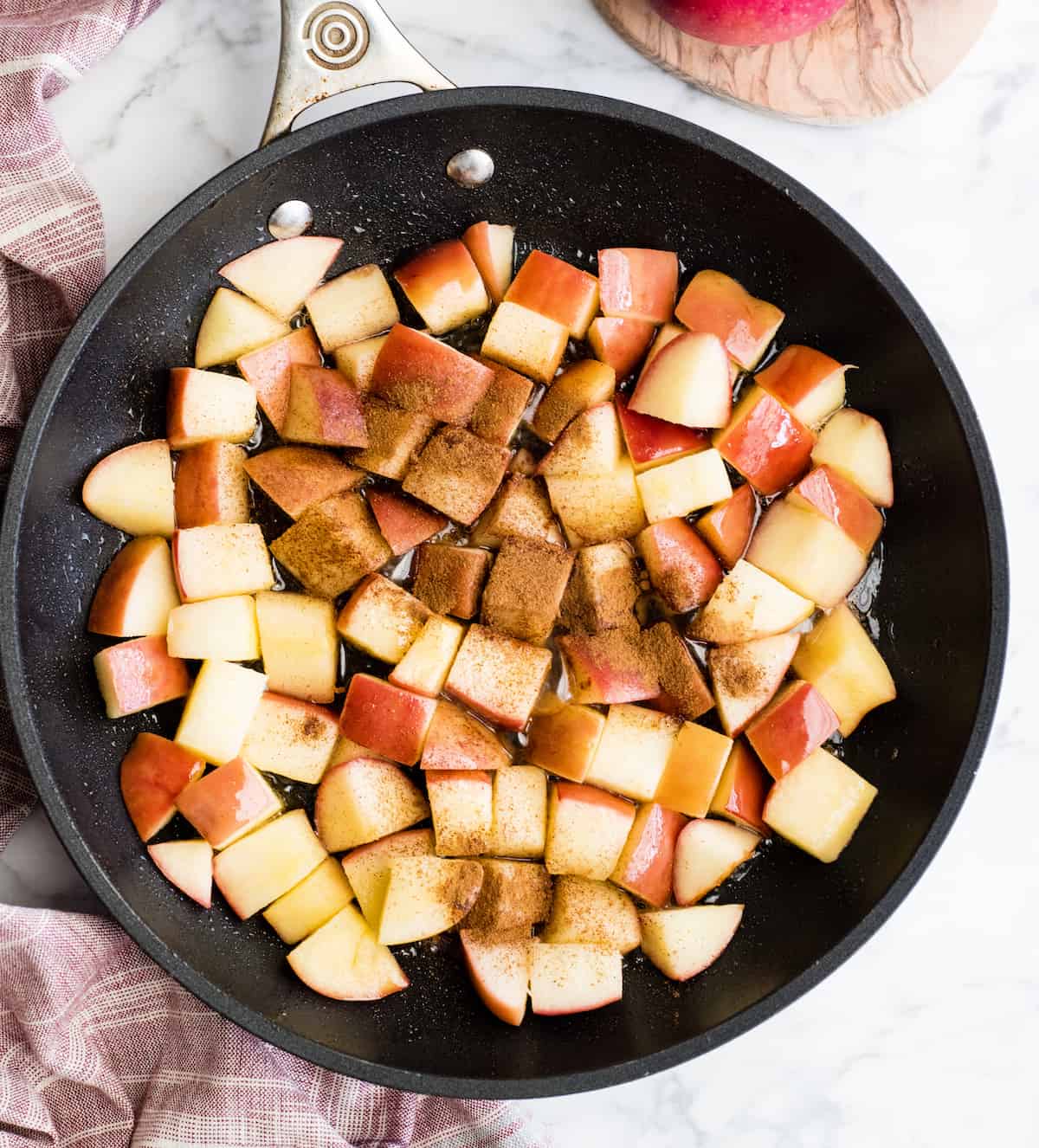 These Stovetop Sautéed Cinnamon Apples taste like a warm apple pie, but they come together in 5 minutes and are SO much healthier! This recipe is gluten-free, dairy-free, refined sugar free, vegan AND paleo! Perfect for breakfast, a snack, or dessert! #apples #stovetop #cinnamon #healthyrecipe #dessert #breakfast #snack #paleo #vegan #glutenfree #dairyfree #refinedsugarfree Overhead view of adding cinnamon to apples in a black fry pan showing how to make cinnamon apples