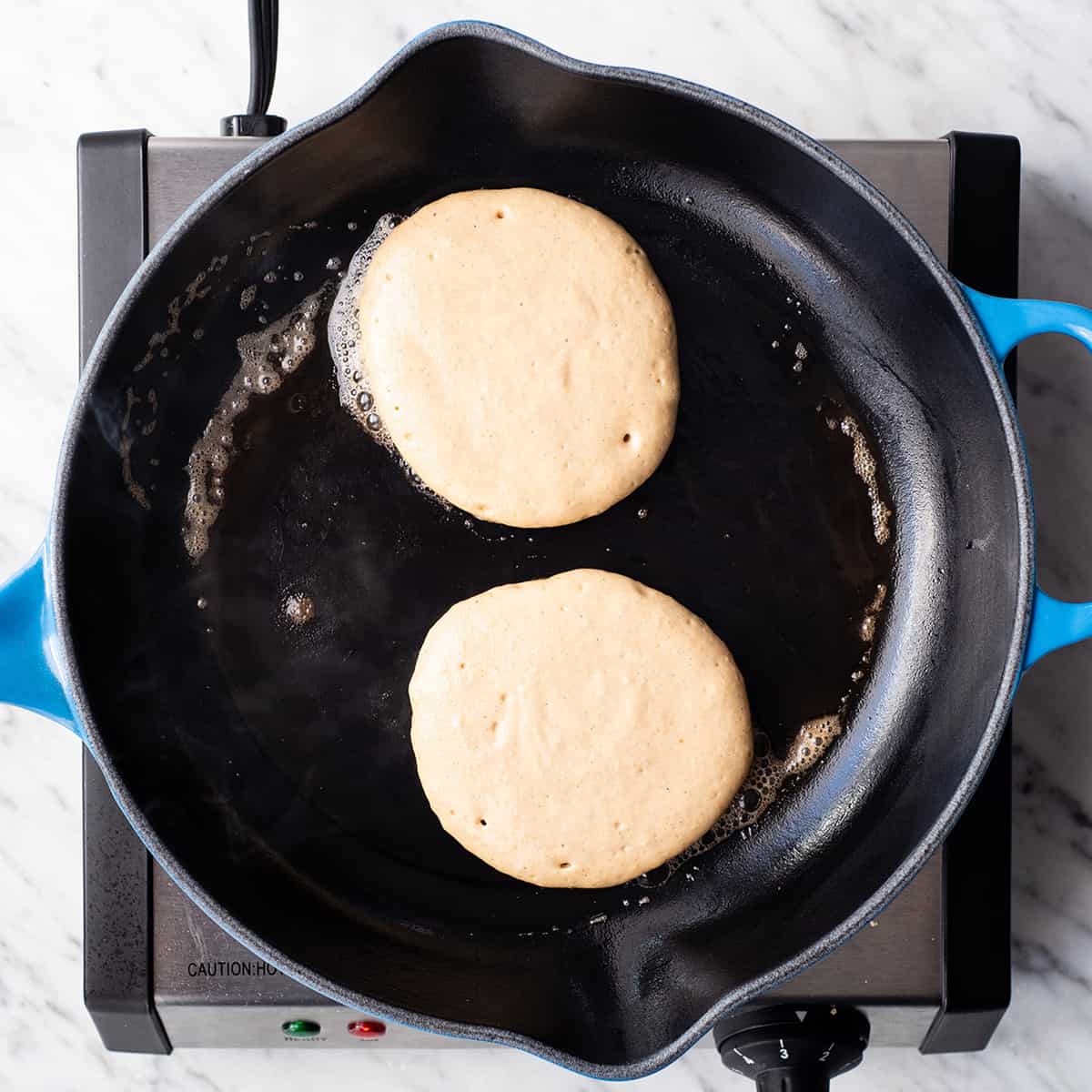 Healthy Greek Yogurt Pancakes! An easy, delicious and nutritious breakfast recipe that your whole family will love! Gluten-free, refined sugar free and freezer-friendly! #glutenfree #pancakes #recipe #greekyogurt #breakfast #vitamix #healthy overhead view of two Greek Yogurt Pancakes cooking in a cast iron skillet before being flipped