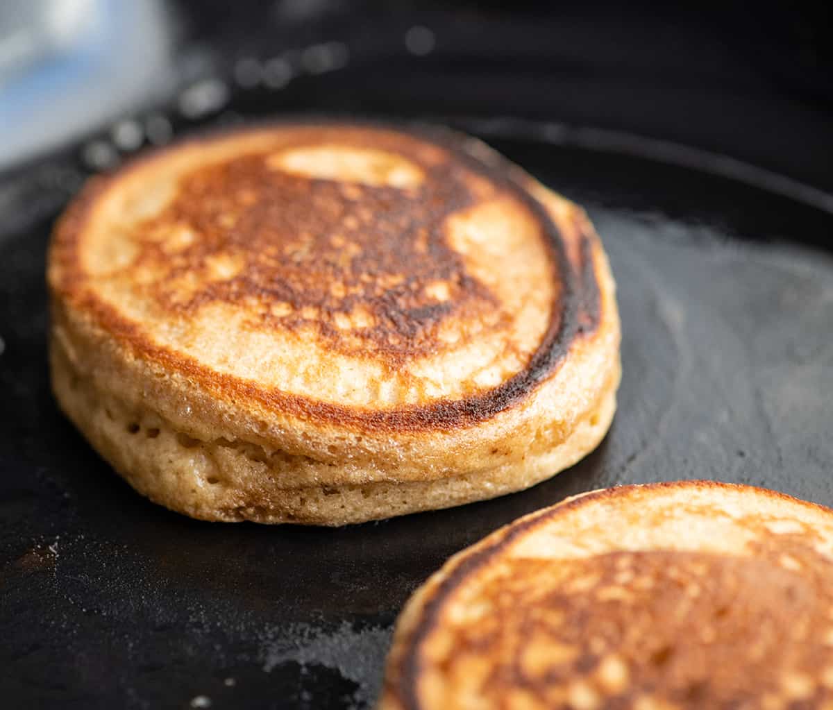 Healthy Greek Yogurt Pancakes Recipe! An easy, one-bowl, delicious and nutritious breakfast recipe that your whole family will love! Freezer-friendly with gluten-free and refined sugar free options!! #easybreakfast #pancakes #recipe #greekyogurt #breakfast #vitamix #healthy front view of a Greek Yogurt Pancake cooking in a cast iron skillet