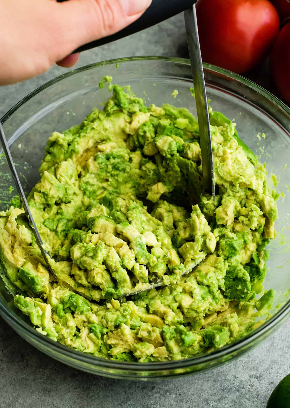 This quick & easy guacamole recipe is made with a handful of healthy ingredients and is ready in 5 minutes! This simple guacamole dip is our favorite appetizer and we always make it on taco nights! Watch the video to learn how to make this guacamole recipe! #guacamole #guacamolerecipe #tacos #appetizer #dip photo showing How to make Guacamole - mashing the avocados