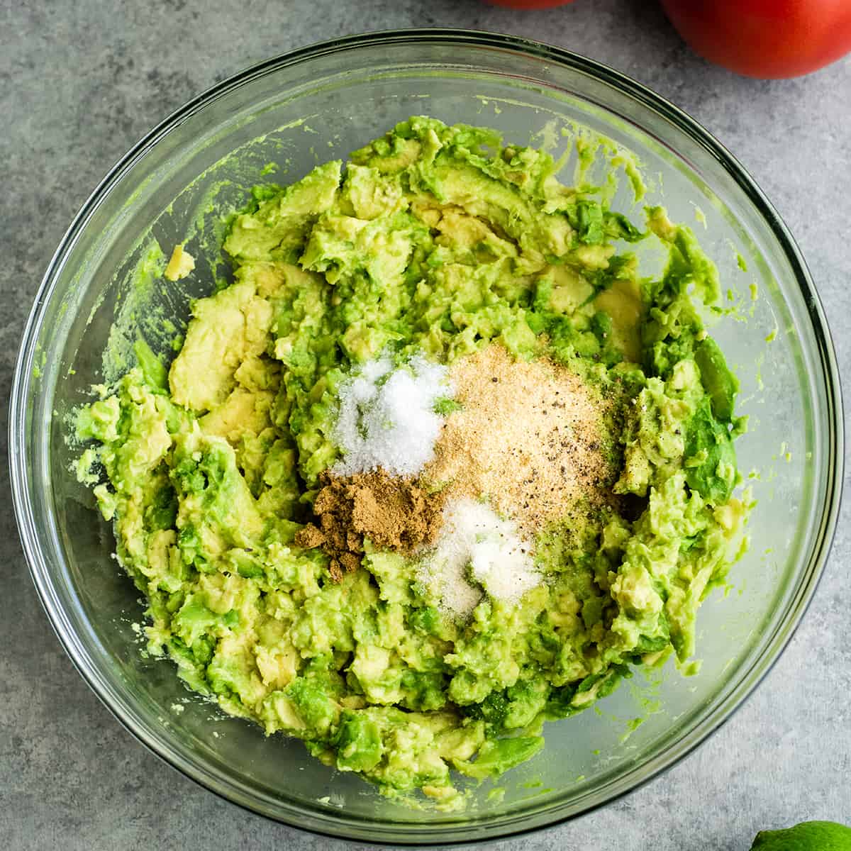 This quick & easy guacamole recipe is made with a handful of healthy ingredients and is ready in 5 minutes! This simple guacamole dip is our favorite appetizer and we always make it on taco nights! Watch the video to learn how to make this guacamole recipe! #guacamole #guacamolerecipe #tacos #appetizer #dip photo showing How to make Guacamole - adding spices and salt
