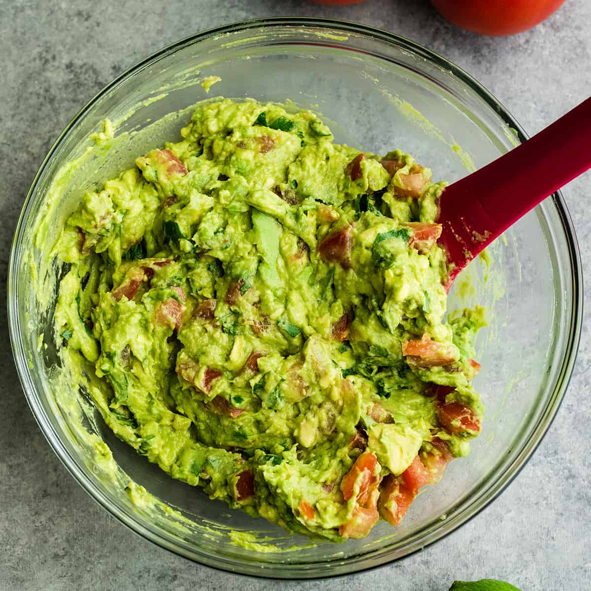 This quick & easy guacamole recipe is made with a handful of healthy ingredients and is ready in 5 minutes! This simple guacamole dip is our favorite appetizer and we always make it on taco nights! Watch the video to learn how to make this guacamole recipe! #guacamole #guacamolerecipe #tacos #appetizer #dip photo showing guacamole mixed in a bowl with a spatula