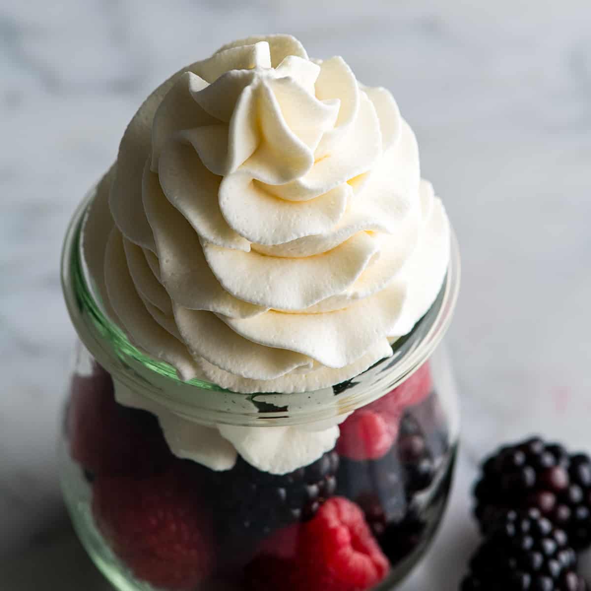 Homemade whipped cream is easy to make with only 3 ingredients in 5 minutes and it's so delicious you'll ditch the store-bought stuff for good once you try it! Watch the video and follow our step-by-step photos to learn how to make the best homemade whipped cream recipe! #whippedcream #heavycream #homeamdewhippedcream #joyfoodsunshine #whippedcreamrecipe Overhead view of homemade whipped cream piped on top of fresh berries