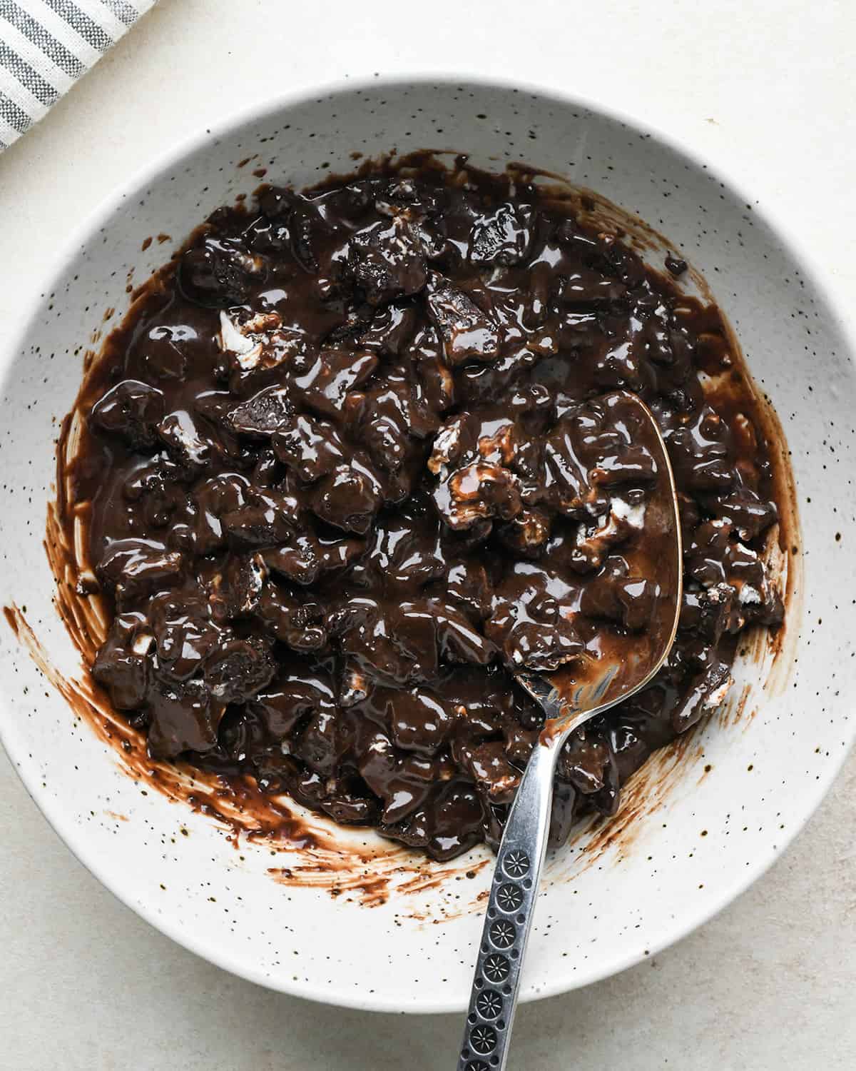 assembling an ice cream cake - chopped oreos mixed with warm chocolate fudge sauce in a bowl