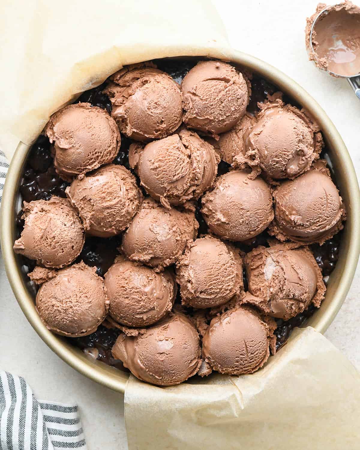 assembling an ice cream cake - ice cream on top of the fudge layer in a cake pan before spreading out
