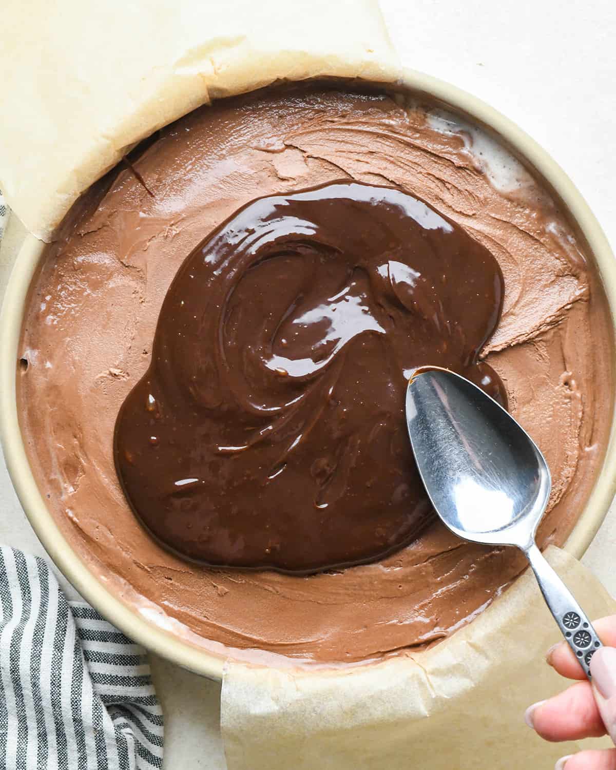 assembling an ice cream cake - fudge sauce on top of the chocolate ice cream layer in a cake pan before spreading out