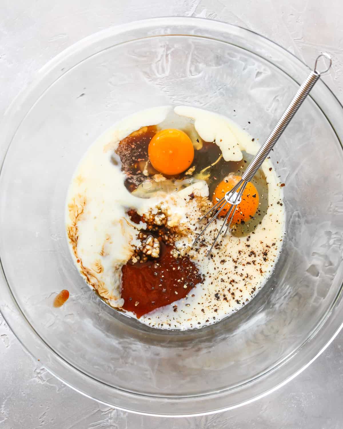 How to Make Meatloaf - wet ingredients in a large glass bowl with a whisk before mixing