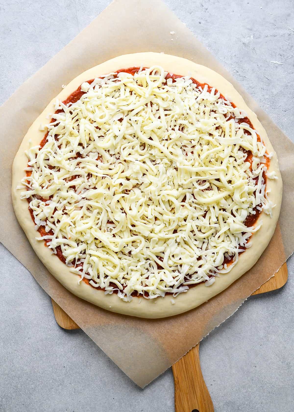 an unbaked pizza made on homemade pizza dough on parchment paper on a wooden pizza peel