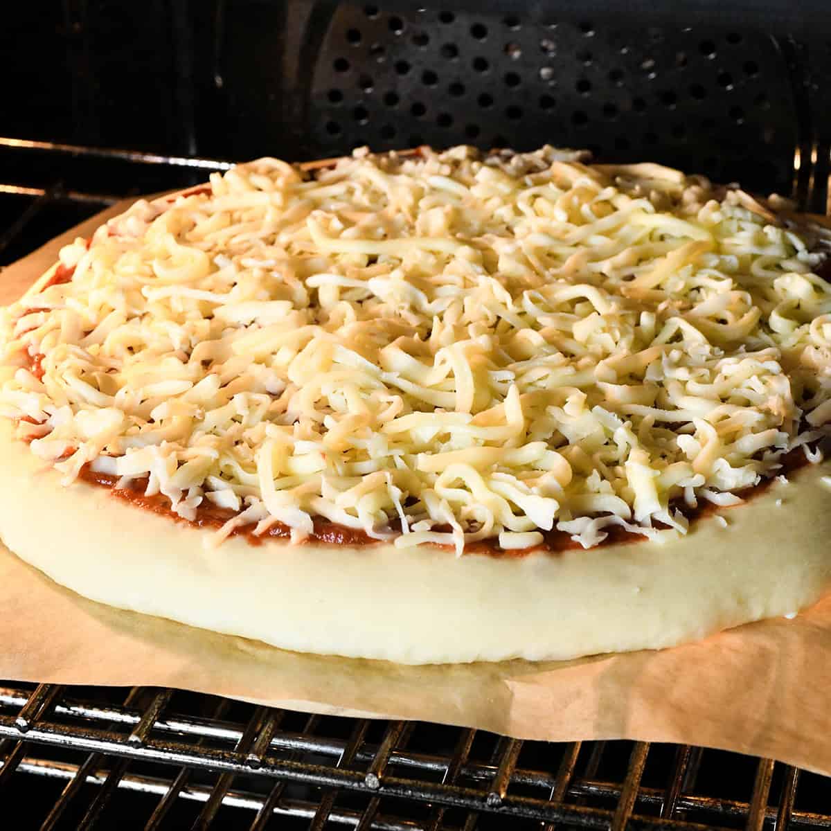 unbaked pizza right in then oven on parchment paper on a pizza stone just after it has been put in the oven.