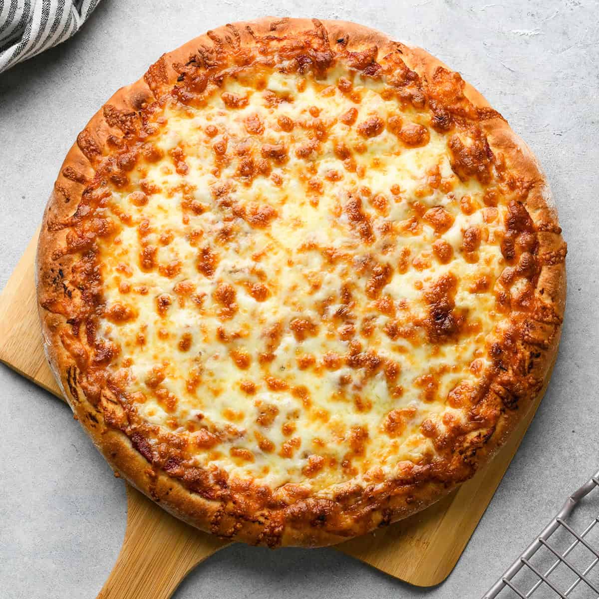 a baked pizza on a pizza peel on a gray surface with a wire cooling rack in the bottom right corner