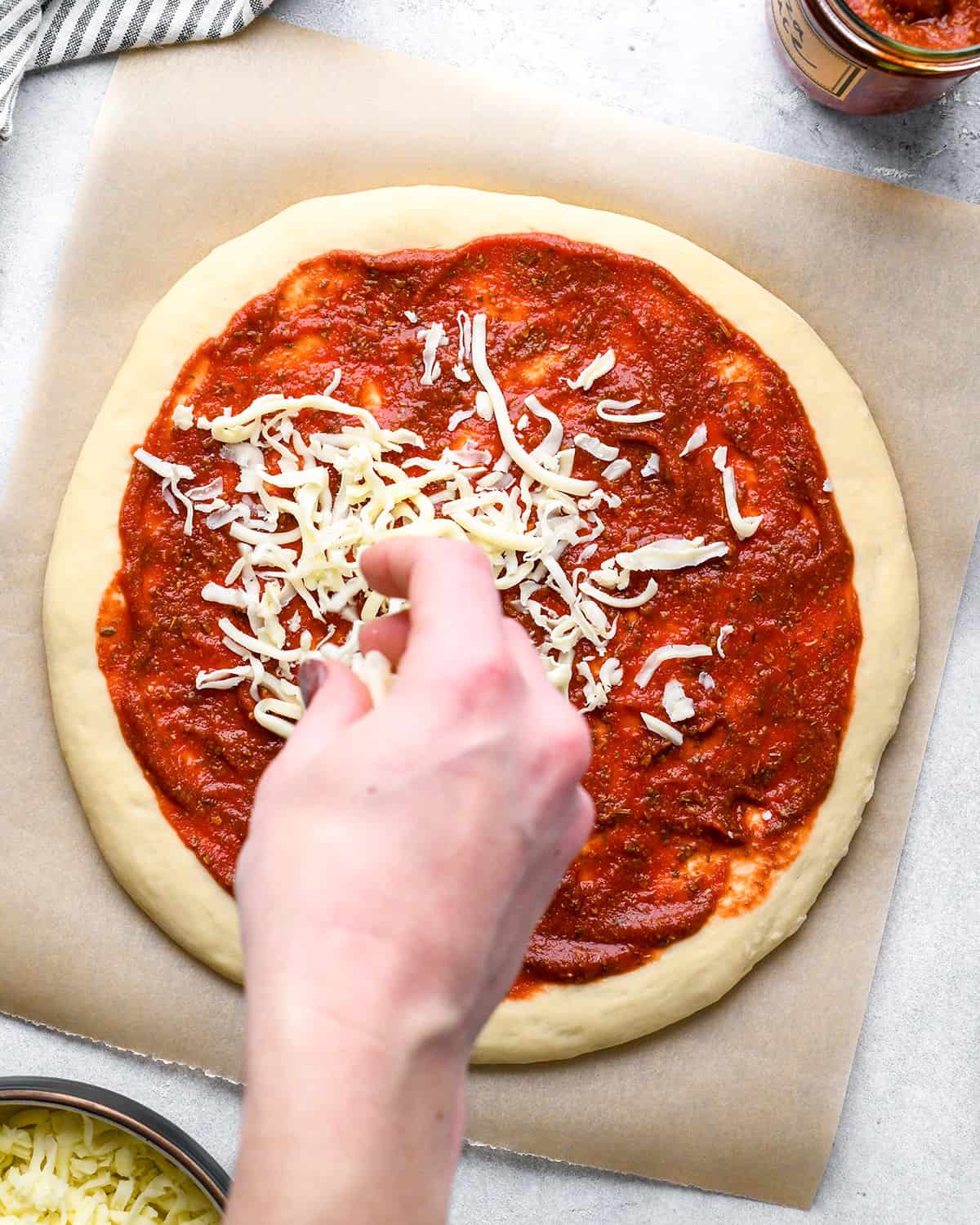 How to Make Pizza a hand sprinkling cheese over the sauce