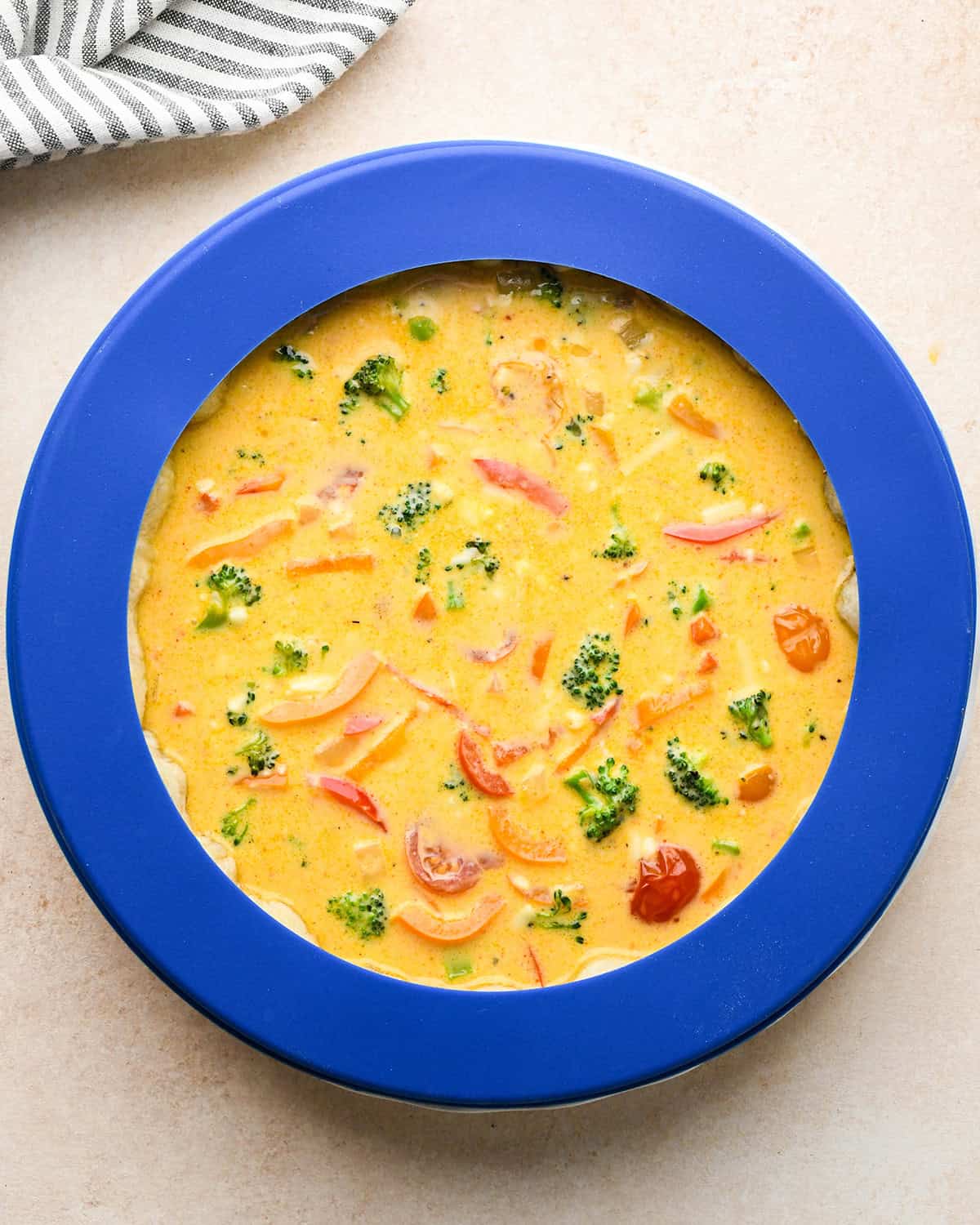 vegetable quiche in a pie dish before baking with a pie crust shield