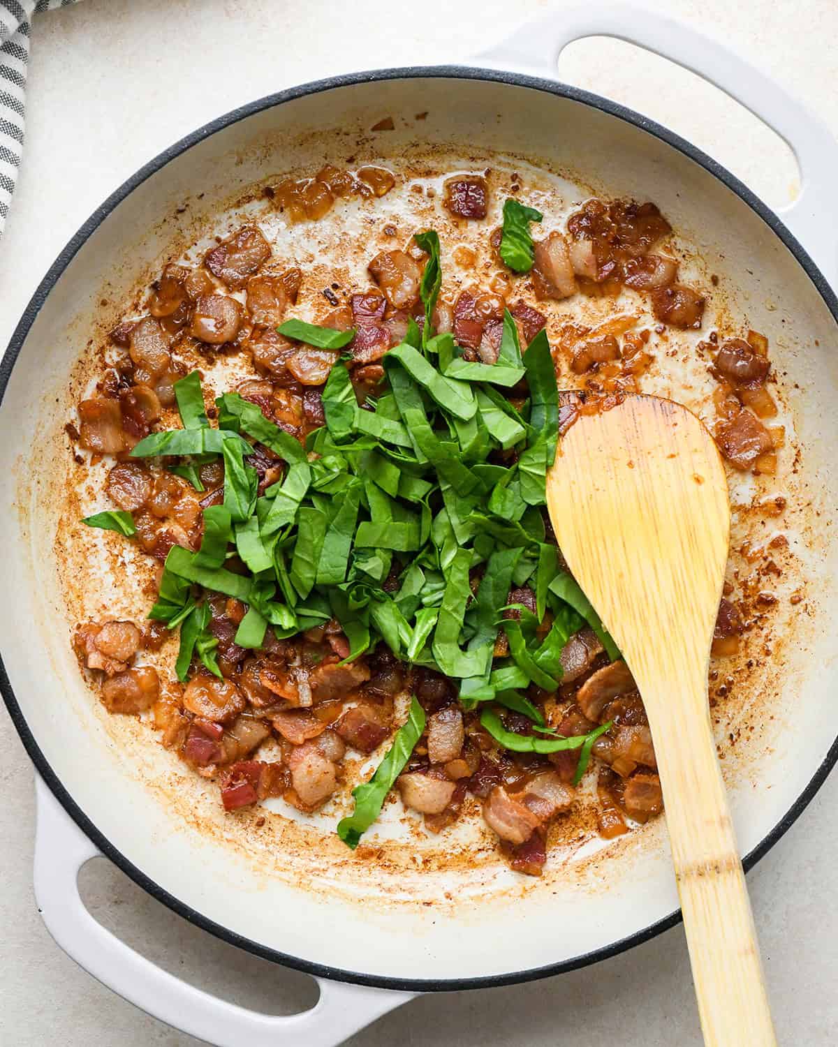 spinach being added to cooked bacon to make bacon spinach quiche