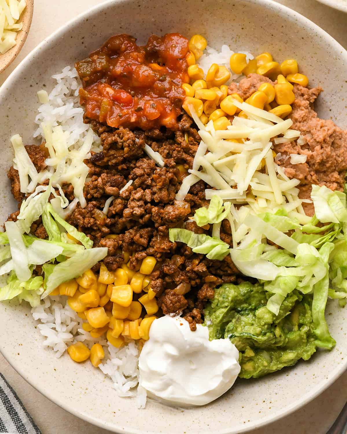 Assembling taco bowls - adding sour cream, salsa, guacamole and lettuce