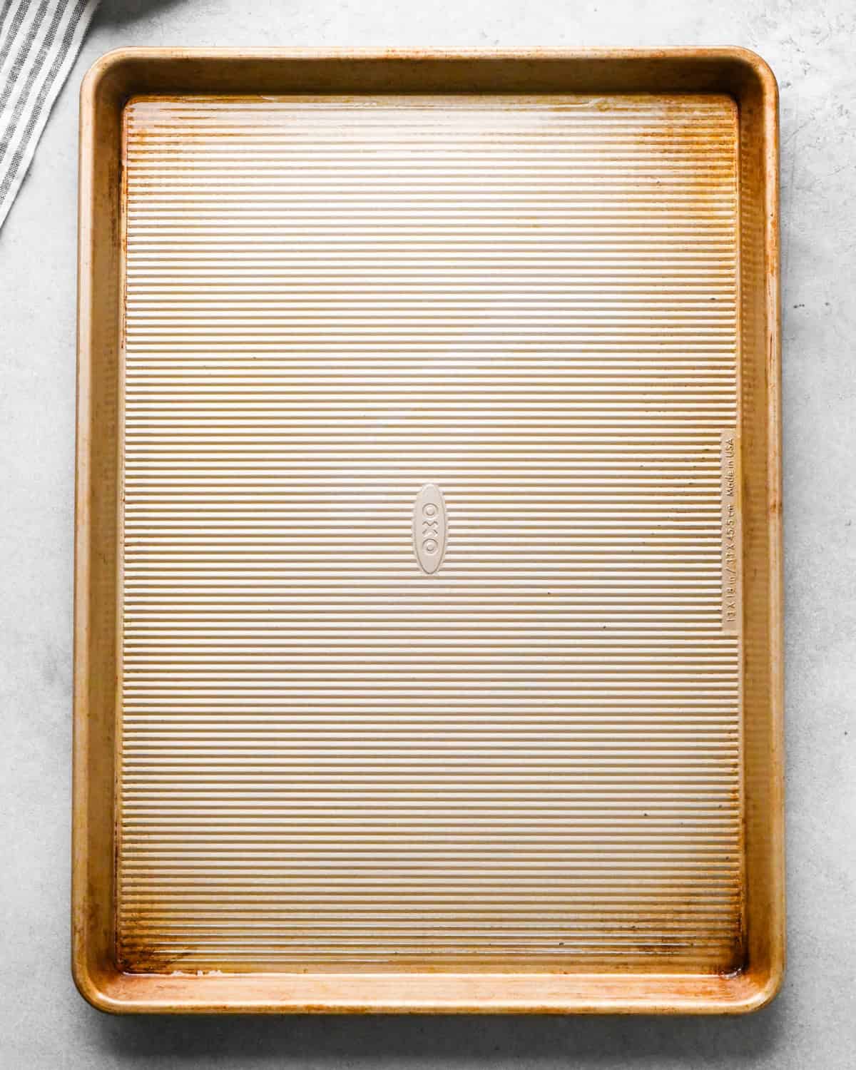 a gold baking sheet greased with olive oil on a gray background with a striped towel in the top left corner