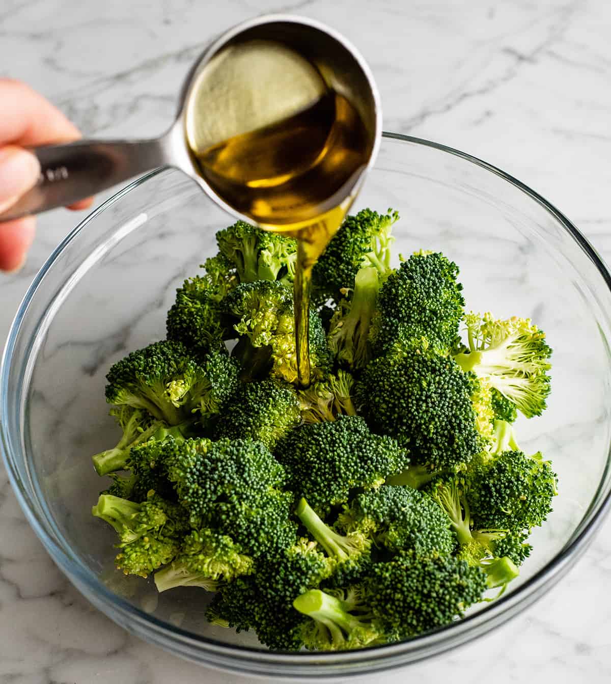 This is the best oven-roasted broccoli recipe! This easy roasted broccoli is made with 6 ingredients in 15 minutes! It's crispy, tender and perfectly seasoned! Baked broccoli is a healthy side dish that pairs well with everything! #broccoli #broccolirecipes #healthysidedish #sidedish #roastedbroccoli #joyfoodsunshine photo showing how to roast broccoli - pouring olive oil over broccoli