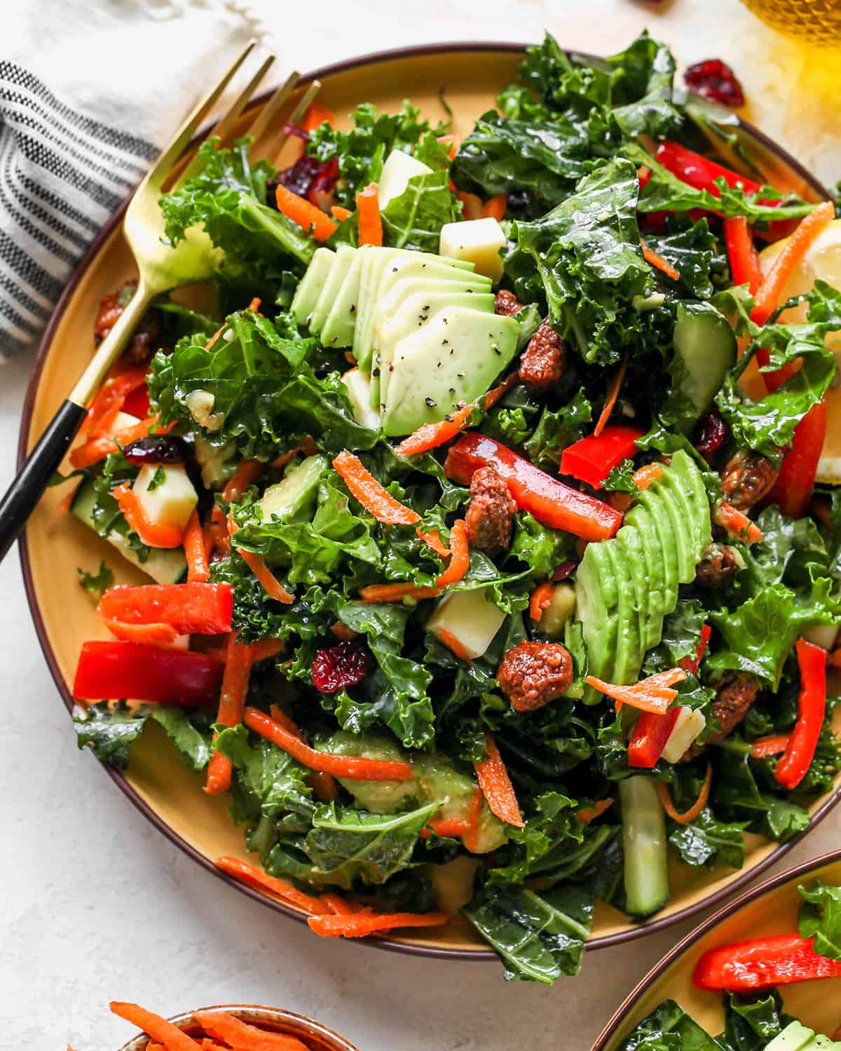 This kale salad recipe is loaded with colorful vegetables, sweet cranberries, crunchy pecans, creamy cheddar cheese and the best homemade dressing ever! It’s a hearty salad that holds up well and will impress even kale skeptics. overhead photo of Kale Salad on a plate