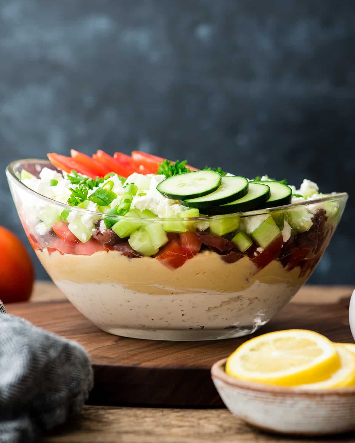 This Layered Greek Dip Recipe is the perfect healthier appetizer to serve when you're entertaining this summer! It's always the hit of the party (or BBQ)! It's gluten-free and only takes 10 minutes of prep time! #recipe #appetizer #healthy #glutenfree #bbq #dip #Greekdip #layereddip Front view of Layered Greek Dip recipe in a glass bowl