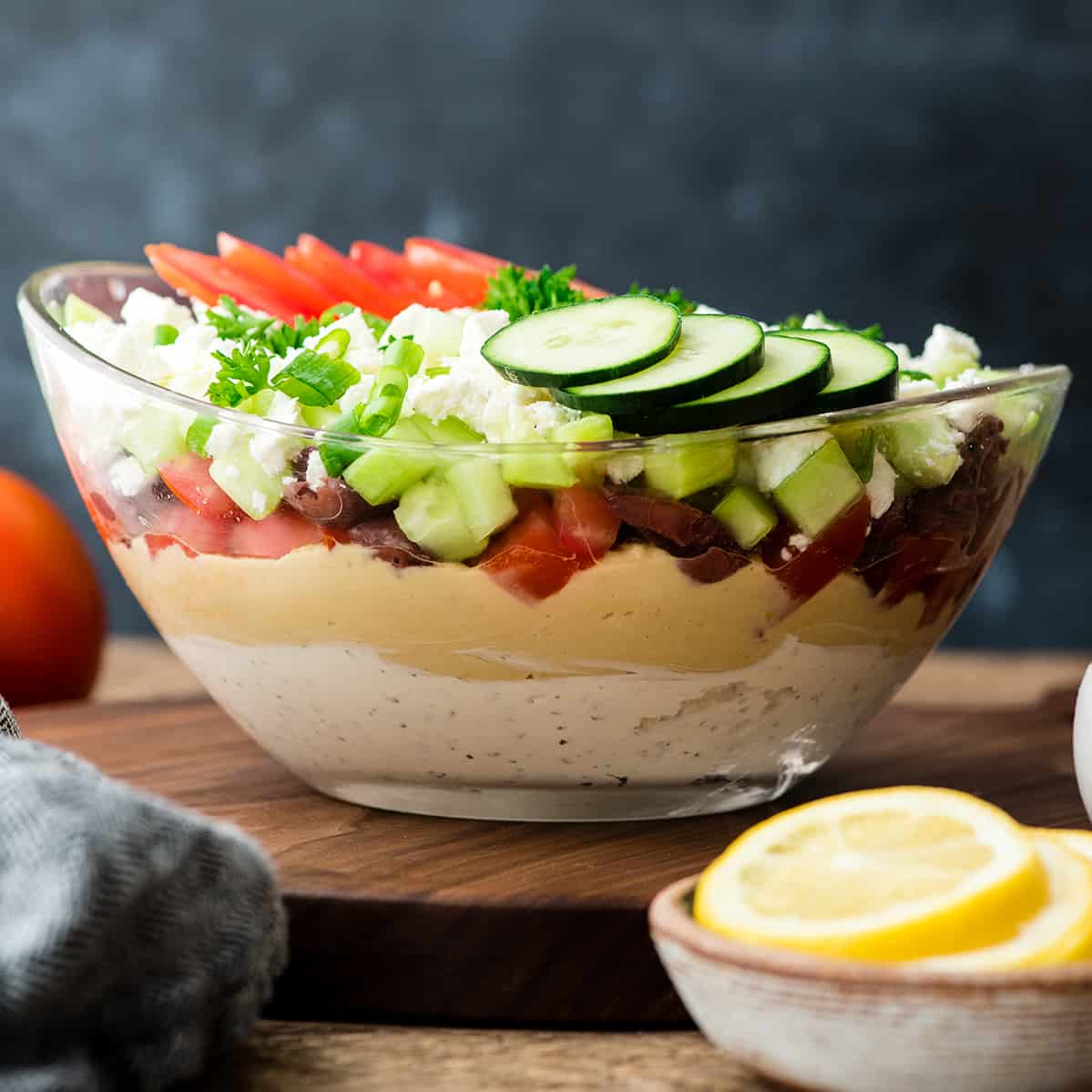 This Layered Greek Dip Recipe is the perfect healthier appetizer to serve when you're entertaining this summer! It's always the hit of the party (or BBQ)! It's gluten-free and only takes 10 minutes of prep time! #recipe #appetizer #healthy #glutenfree #bbq #dip #Greekdip #layereddip Front view of Layered Greek Dip recipe in a glass bowl