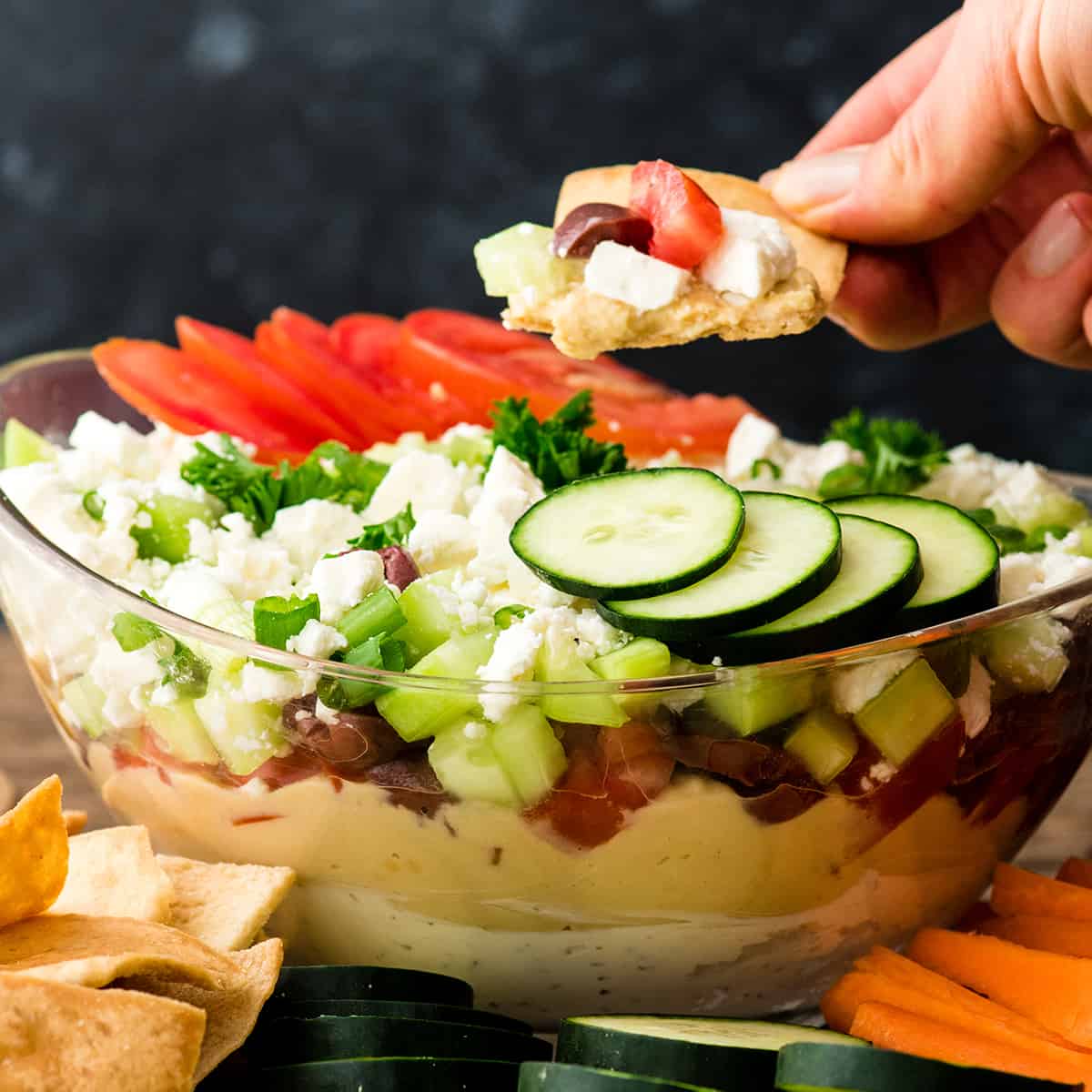 a hand holding a pita chip with some Greek dip on it
