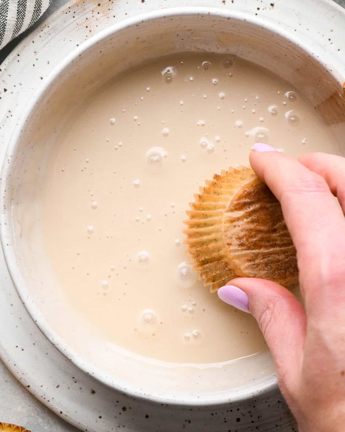 a Lemon Poppy Seed Muffin being dipped into a bowl of glaze
