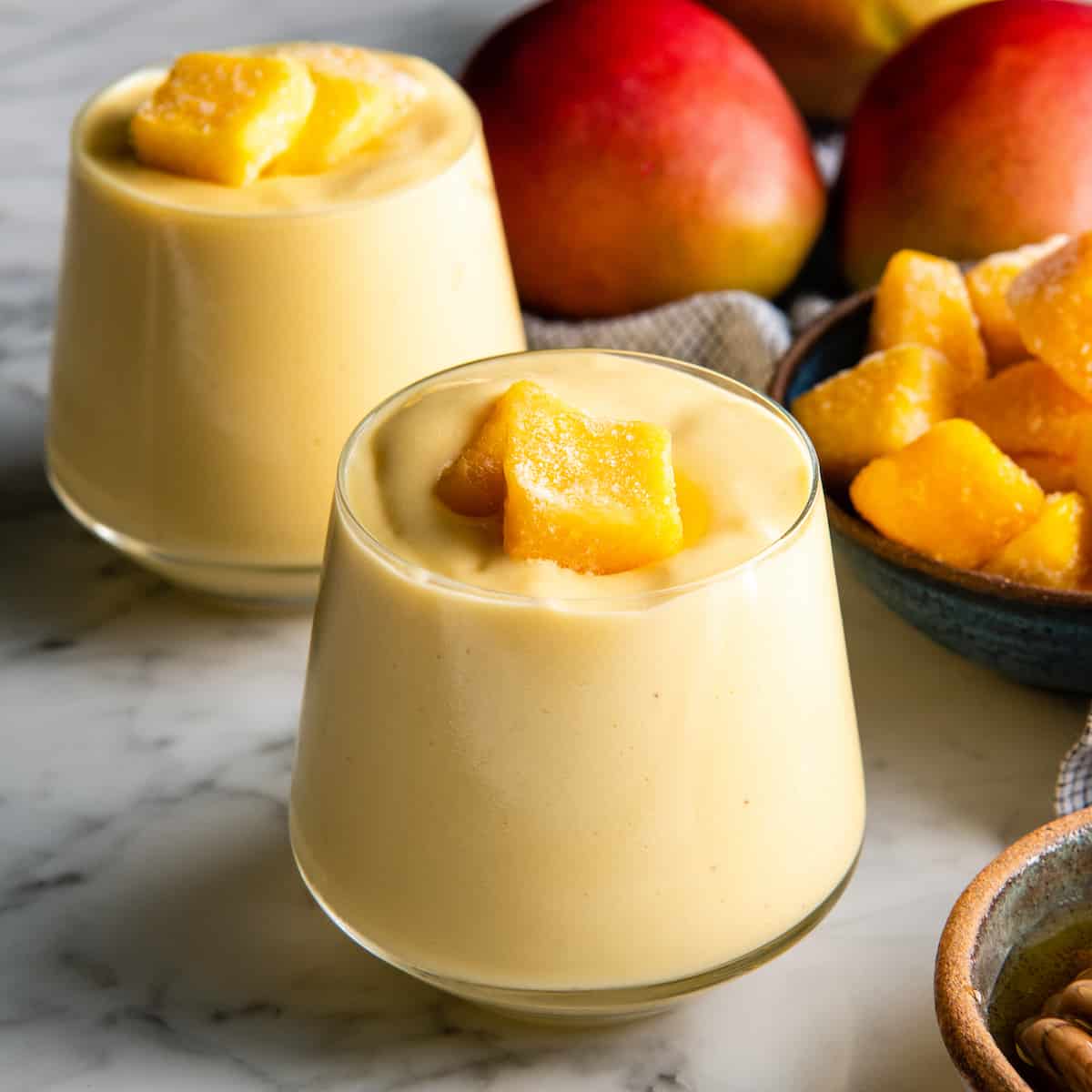 The BEST mango smoothie recipe! This healthy & easy mango smoothie is made in 5 minutes with 6 ingredients (including coconut milk, yogurt and banana)! It's ultra creamy and you can use fresh or frozen mango and easily make it dairy-free! #smoothie #mango #mangosmoothie #healthy #recipe #joyfoodsunshine two glasses of mango smoothie with mango chunks on top