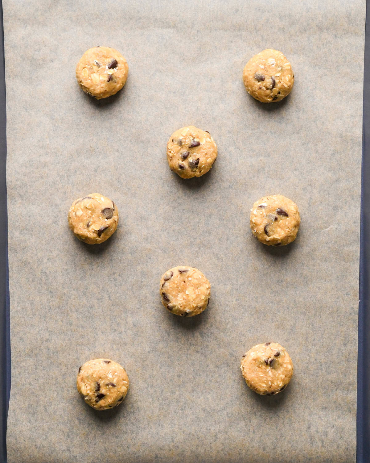 8 oatmeal chocolate chip cookies on a baking sheet lined with parchment paper with the tops slightly impressed down before baking