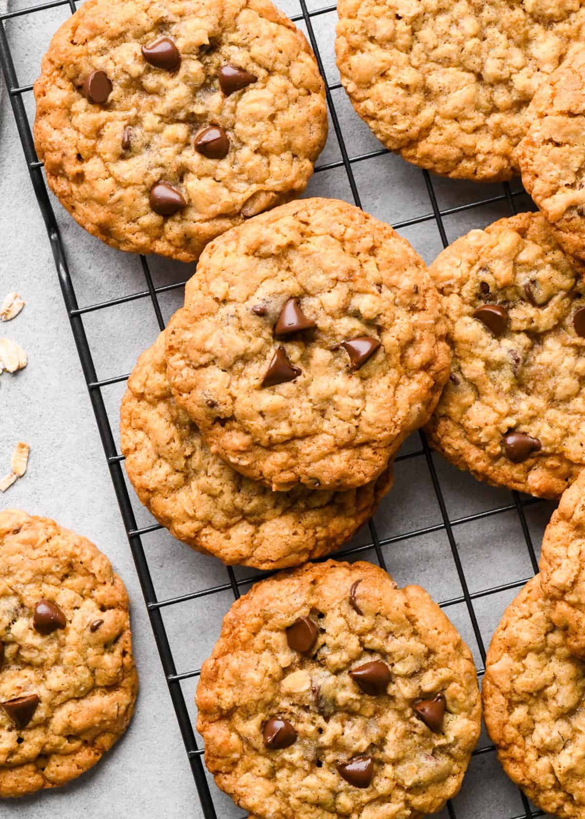 10 Oatmeal Chocolate Chip Cookies on a wire cooling rack on a gray surface with raw oats on nearby