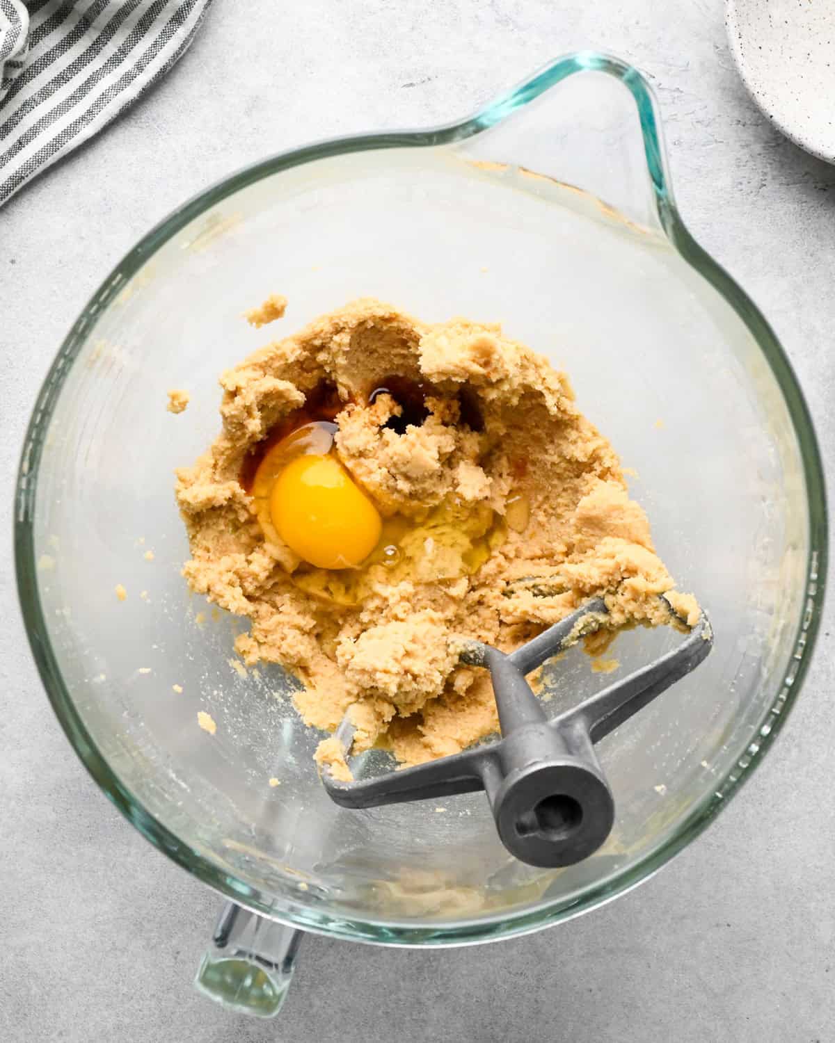 making chocolate chip oatmeal cookies - egg and vanilla added to the beaten butter and sugar mixture in a glass bowl with a paddle attachement before mixing