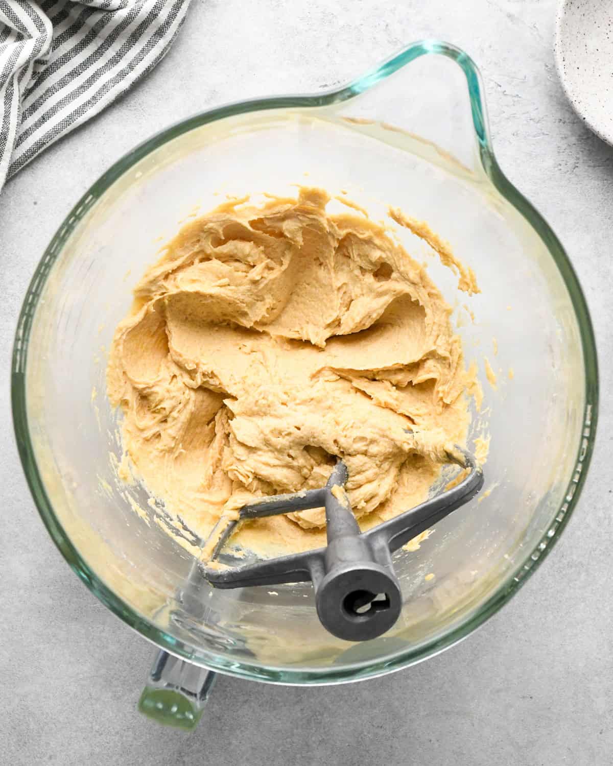 making chocolate chip oatmeal cookies - beaten butter, sugar, egg and vanilla mixture in a glass mixing bowl with a paddle attachement and a striped towel in the top left corner.