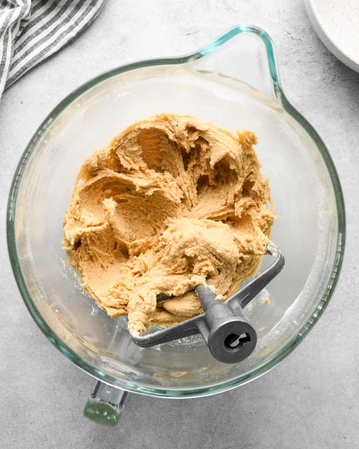 making chocolate chip oatmeal cookies - dough after wet and dry ingredients have been beaten together in a glass mixing bowl with a paddle attachement and a striped towel and bowl nearby