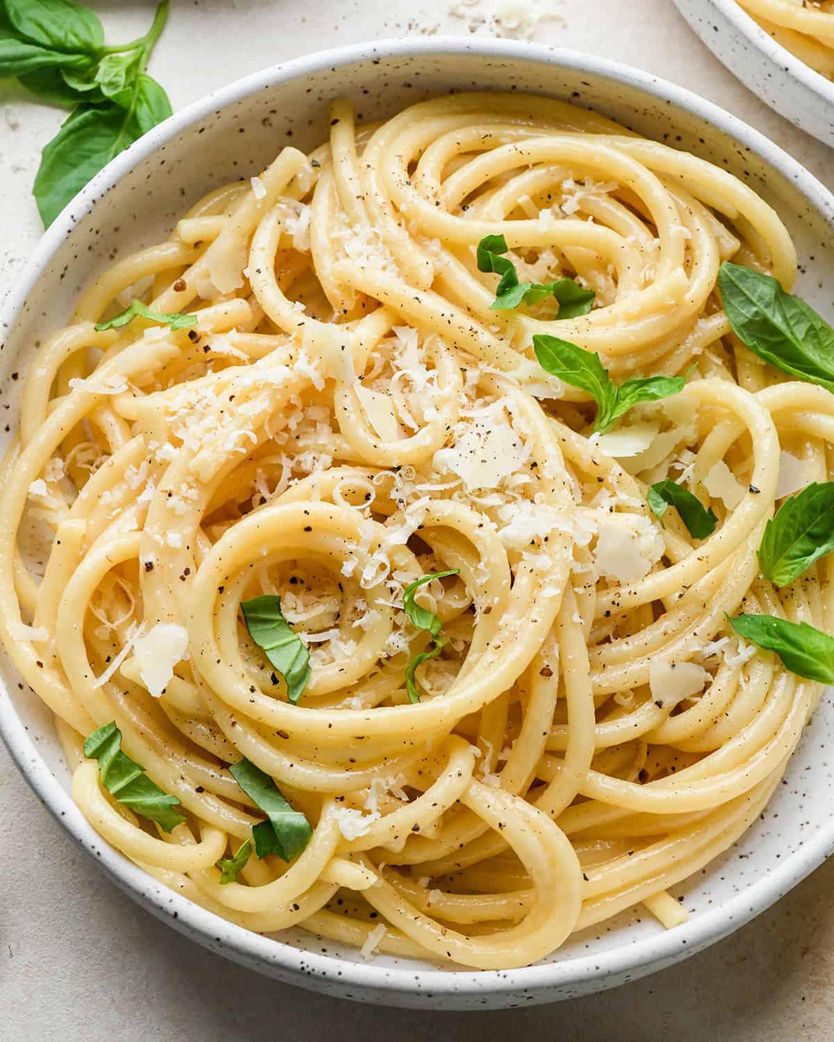 Parmesan Pasta in a bowl topped with fresh basil, parmesan cheese and pepper.