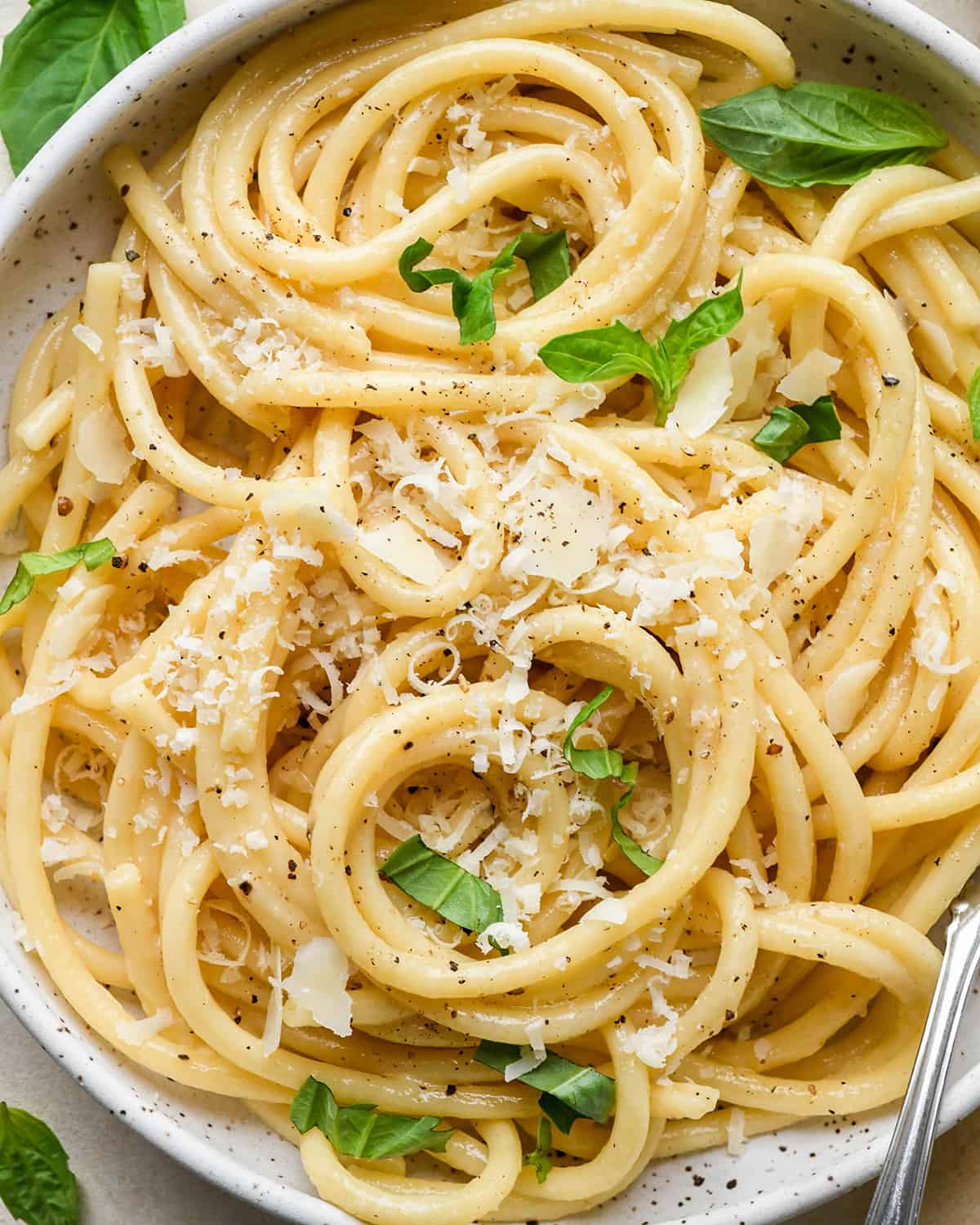 Parmesan Pasta in a bowl topped with fresh basil, parmesan cheese and pepper.