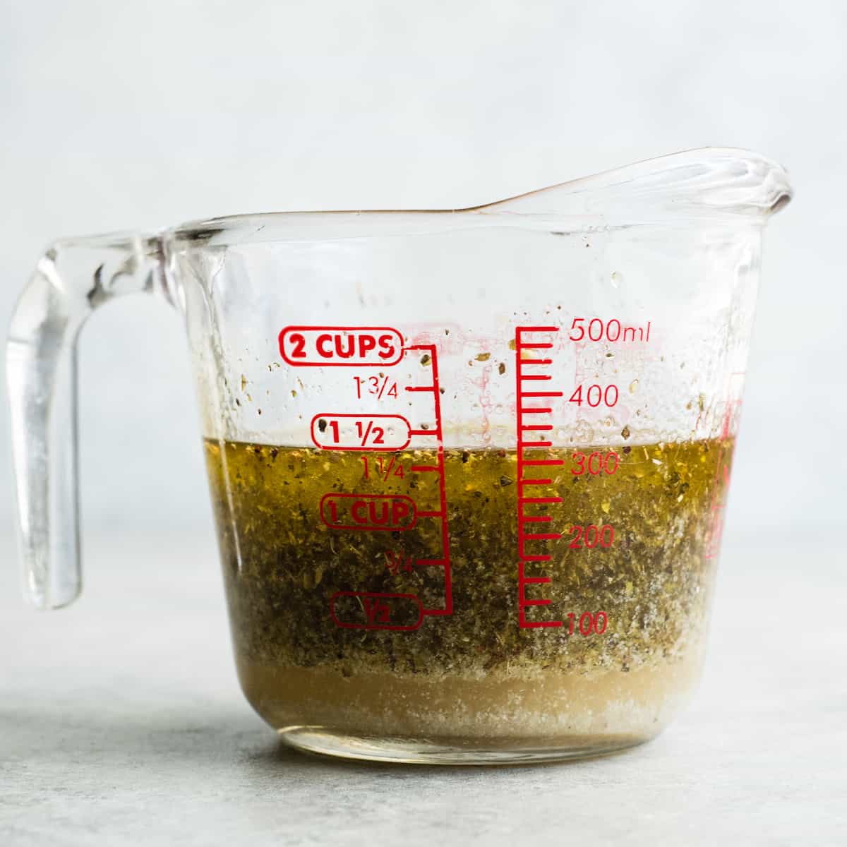 This Best Pasta Salad Recipe is made with Homemade Dressing & Roasted Tomatoes! It is the perfect healthy & flavorful make-ahead BBQ side dish full of fresh veggies, pepperoni and fresh mozzarella cheese! Gluten-free & Vegan options! #pastasalad #bbq #sidedish #bestpastasalad #pastasaladrecipe #recipe #healthyrecipe #glutenfree #vegan front view of a glass container with the homemade pasta salad dressing