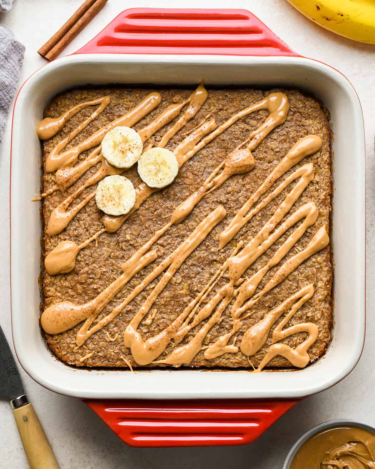 Peanut Butter Banana Baked Oatmeal in a baking dish drizzled with peanut butter, topped with sliced bananas and cinnamon