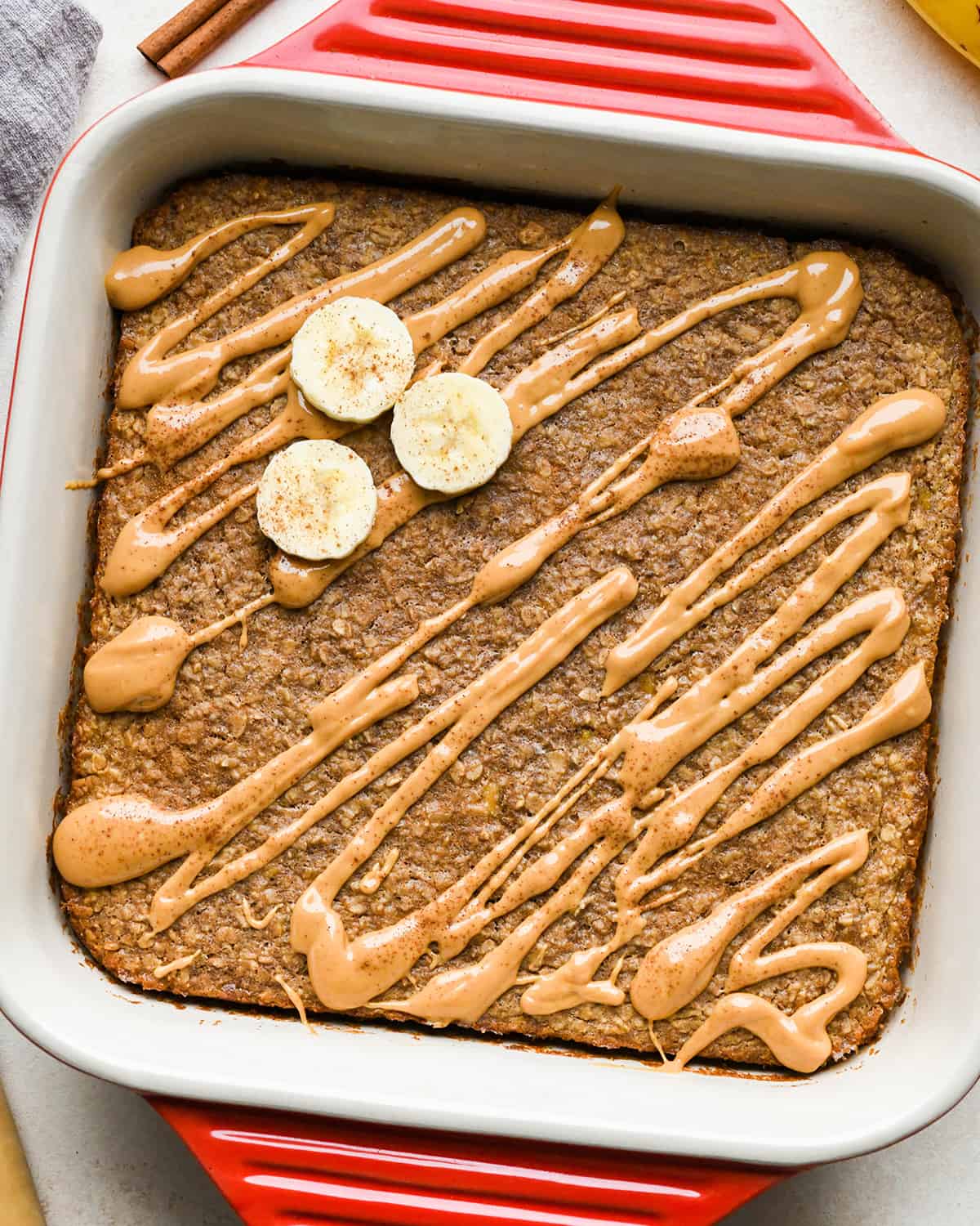 This Healthy Peanut Butter Banana Baked Oatmeal is the perfect make-ahead breakfast recipe! It's gluten-free, dairy-free, & vegan-friendly with no refined sugar! #peanutbutter #bakedoatmeal #banana #breakfast #recipe #glutenfree #dairyfree #veganfriendly #kidfriendly #healthyrecipe Peanut Butter Banana Baked Oatmeal in a baking dish drizzled with peanut butter, topped with sliced bananas and cinnamon
